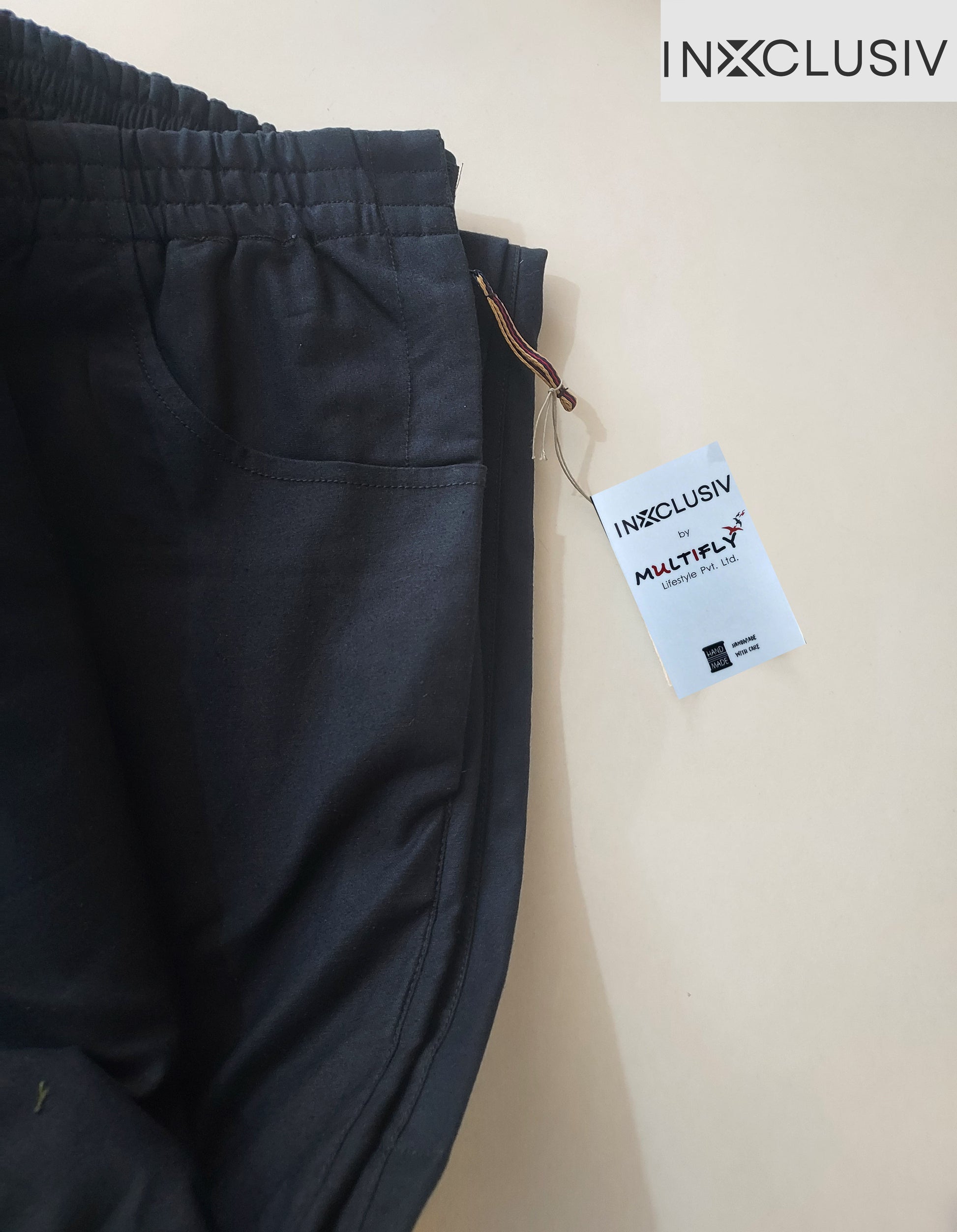 The trouser is half fold from the centre. here both the side seams are alligned with each other. scoop pocket, zipper puller tab and tag is visible. There is a brand logo on the right hand top corner of the picture.