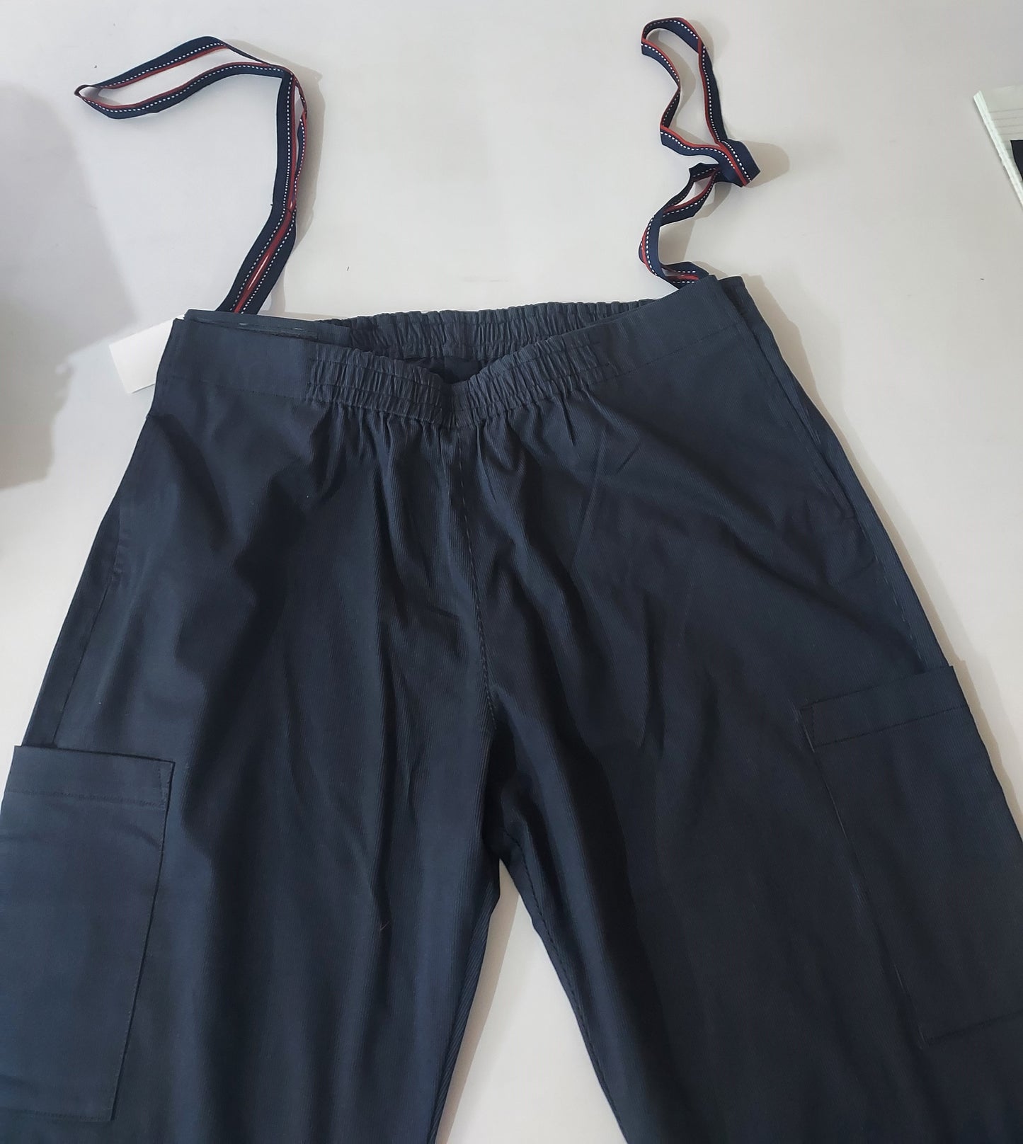 In this photo, the trouser is laid flat on a white surface. one can see two patch pockets on the thigh area on both the sides. elastic on the back and front. there are two loops to help the wearer pull up the trousers and also the caregiver can use the same to help the wearer. 